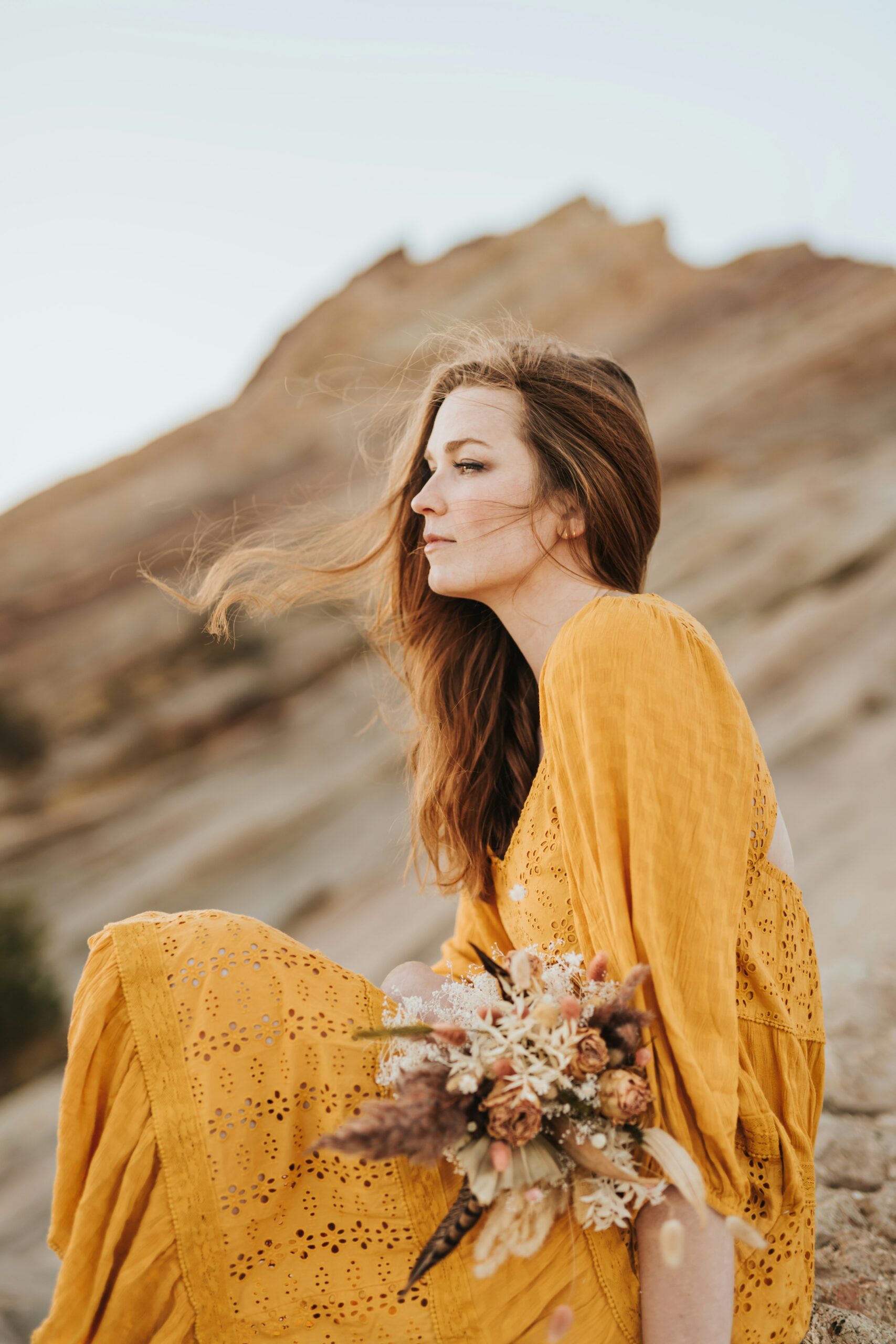 Woman sitting outdoors in natural light with a thoughtful expression, reflecting on emotional reactions and nervous system patterns.